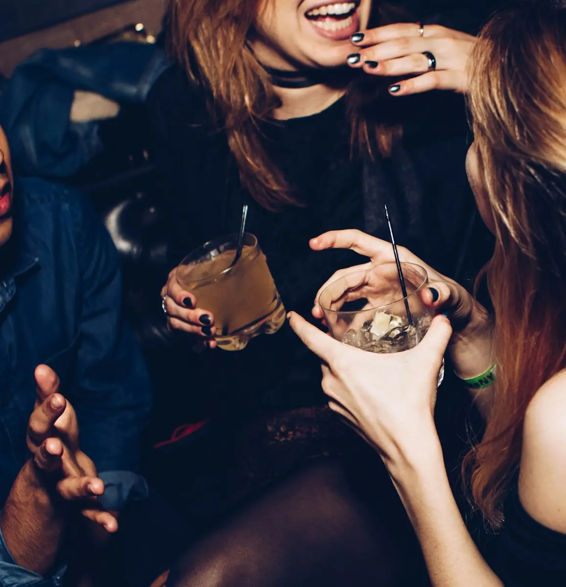 Three friends laughing over drinks at a party
